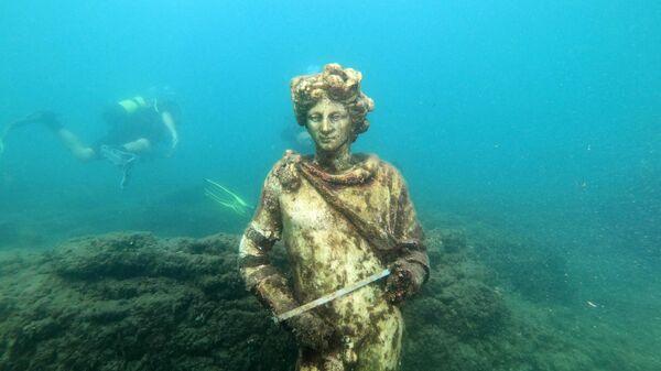 In this photograph taken on August 18, 2021 a dive guide shows tourists a copy of the original statue preserved at the Museum of Baiae, representing Dionysus with ivy crown in the Nymphaeum of punta Epitaffio, the submerged ancient Roman city of Baiae at the Baiae Underwater Park, part of the Campi Flegrei Archaeological Park complex site in Pozzuoli near Naples.  - Sputnik International