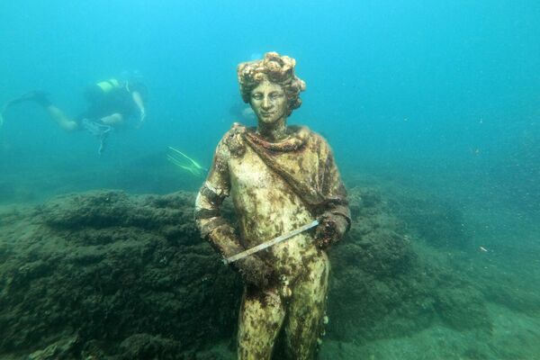 In this photograph taken on August 18, 2021 a dive guide shows tourists a copy of the original statue preserved at the Museum of Baiae, representing Dionysus with ivy crown in the Nymphaeum of punta Epitaffio, the submerged ancient Roman city of Baiae at the Baiae Underwater Park, part of the Campi Flegrei Archaeological Park complex site in Pozzuoli near Naples. Statues which once decorated luxury abodes in this beachside resort are now playgrounds for crabs off the coast of Italy, where divers can explore ruins of palaces and domed bathhouses built for emperors.  - Sputnik International