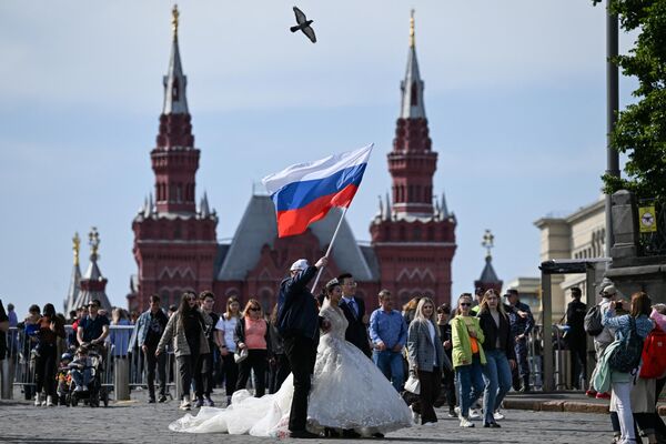 A man waves a Russian flag next to a couple in wedding attire after the patriotic concert at Red Square in downtown Moscow ahead of Russia Day on June 11, 2023. - Sputnik International