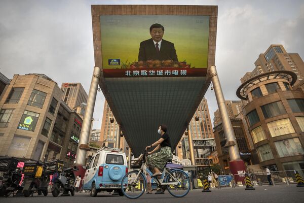 A woman wearing a face mask rides a bicycle past a large television screen at a shopping center displaying Chinese state television news coverage of Chinese President Xi Jinping's visit to Hong Kong in Beijing - Sputnik International
