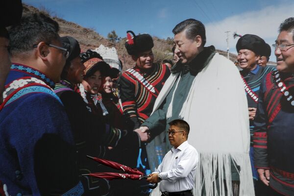 A man carrying umbrellas walks by a photo showing Chinese President Xi Jinping meeting with ethnic minorities on display at a hotel in Chengdu in southwest China&#x27;s Sichuan province. - Sputnik International