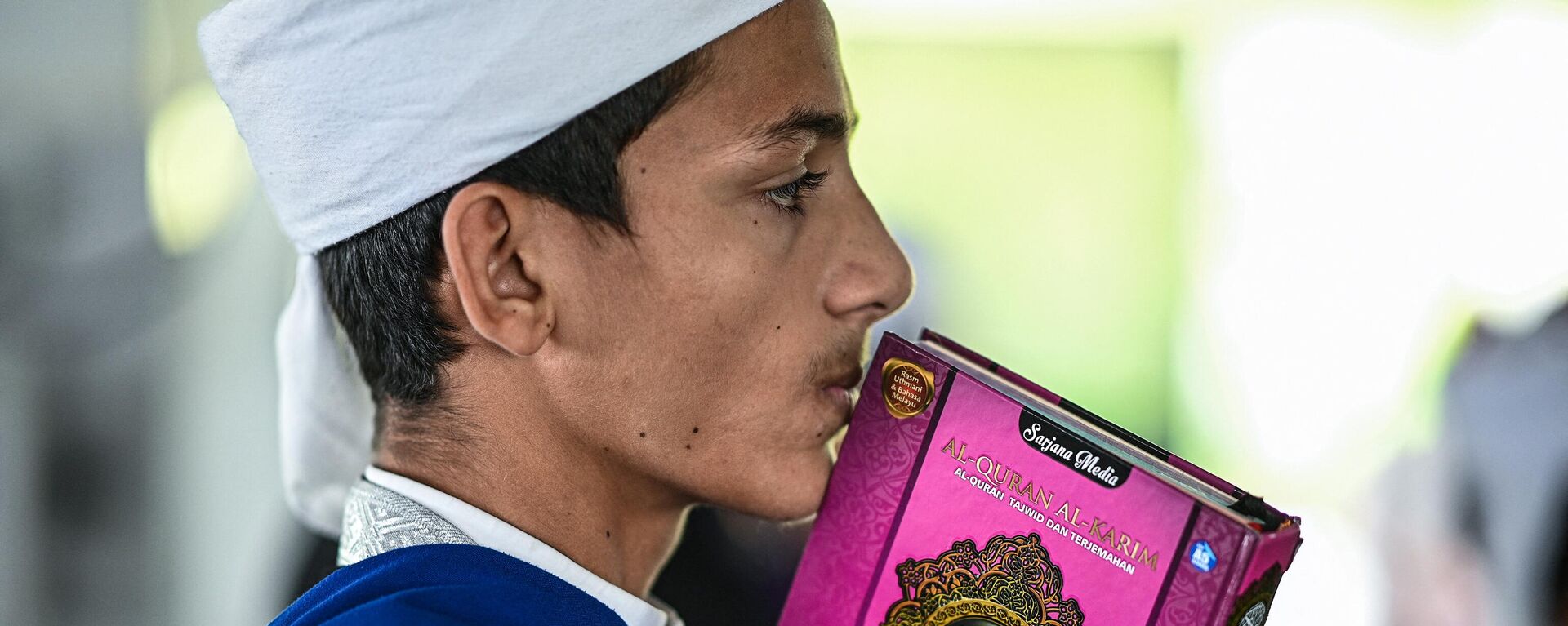 A religious Muslim student kissing a copy of the holy Quran while observing Nuzul Quran. - Sputnik International, 1920, 29.06.2023