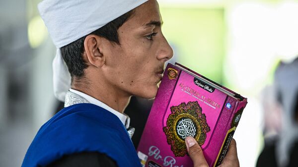 A religious Muslim student kissing a copy of the holy Quran while observing Nuzul Quran. - Sputnik International