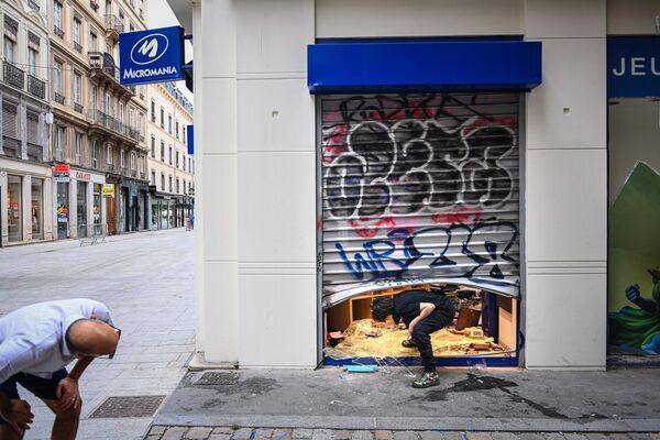 A pedestrian (L) looks at an employee (R) entering in a looted shop.  - Sputnik International