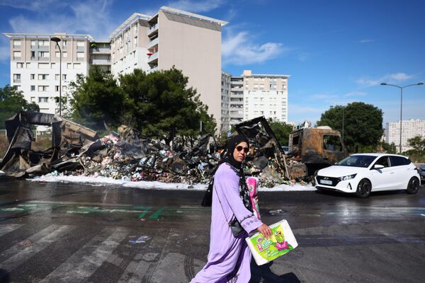A pedestrian walks past a damaged and burnt merchandise truck near an Aldi store in the Les Flamants neighbourhood, in the north of Marseille, southern France.  - Sputnik International