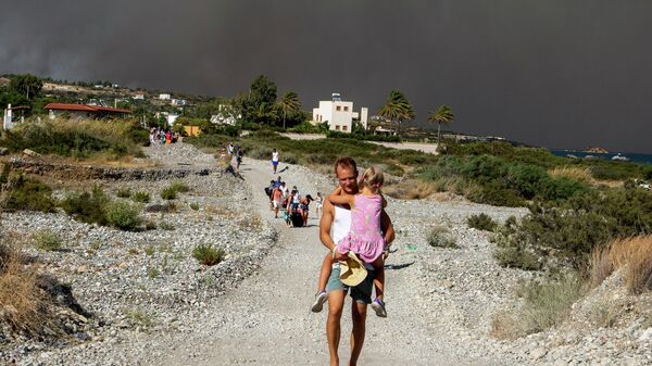 A man carries a child as they leave an area where a forest fire burns, on the island of Rhodes, Greece, Saturday, July 22, 2023.  - Sputnik International