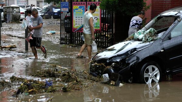 Residents walk near a vehicle damaged and left stranded by flood waters in the Mentougou district on the outskirts of Beijing, Tuesday, Aug. 1, 2023. - Sputnik International