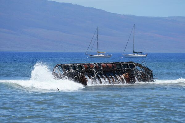 Waves crash over a burnt boat sitting in waters near the former Hawaii capital.  - Sputnik International