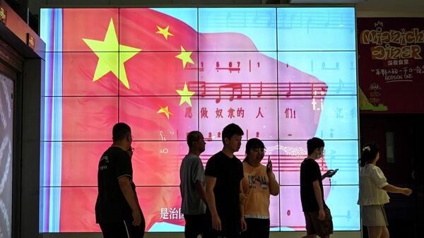 People walk past a screen showing a Chinese national flag at a shopping mall in Beijing on May 26, 2023 - Sputnik International