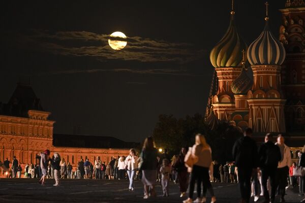 The August Super Blue Moon sets behind a historical building and the St. Basil&#x27;s Cathedral, right, as people walk in Red Square in Moscow, Russia, Wednesday, Aug. 30, 2023. - Sputnik International