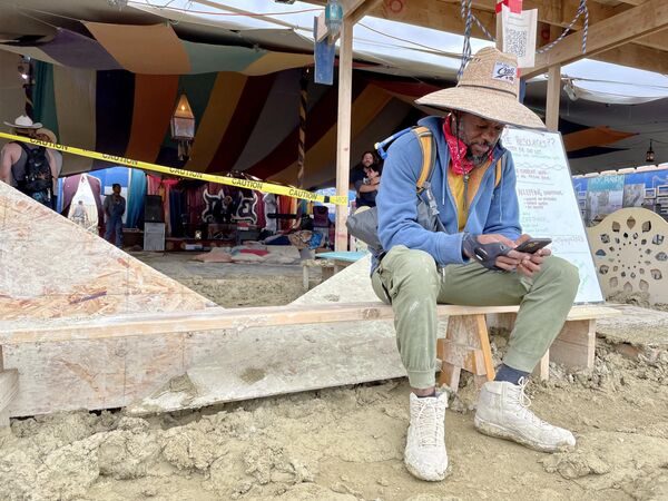 Willonius Hatcher, 39, comedian, screenwriter, and AI content creator checks his phone at Black Rock City Burning Man on September 3, 2023 after rain turned the annual gathering into a quagmire. (Photo by Julie JAMMOT / AFP) - Sputnik International
