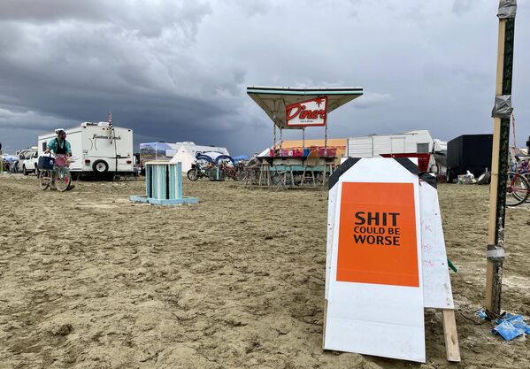 A sign reading &quot;Sh*t Could Be Worse&quot; as campers sit in the mud-covered site of the annual Burning Man festival in Nevada’s Black Rock desert on September 3, 2023. (Photo by Julie JAMMOT / AFP) - Sputnik International
