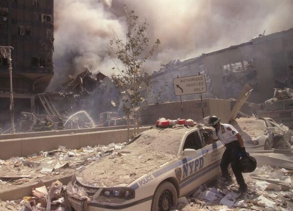 A rescue worker reaches into a New York Police car covered in debris while New York City firefighters douse the smoldering ruins in the background. - Sputnik International