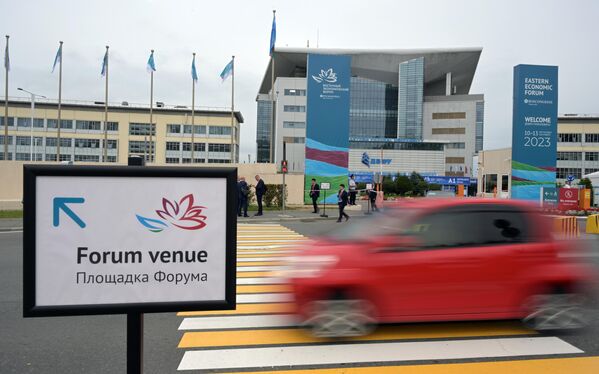 Participants of the EEF stand near the forum venue as a red car drives by. - Sputnik International