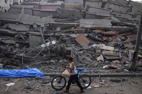 A Palestinian child walks with a bicycle by the rubble of a building after it was hit by an Israeli airstrike on Gaza. - Sputnik International