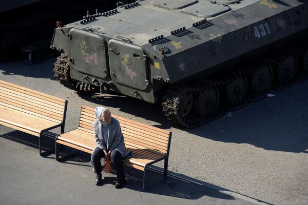 A woman enjoys a sunny day on a bench beside a captured Ukrainian armored vehicles. - Sputnik International