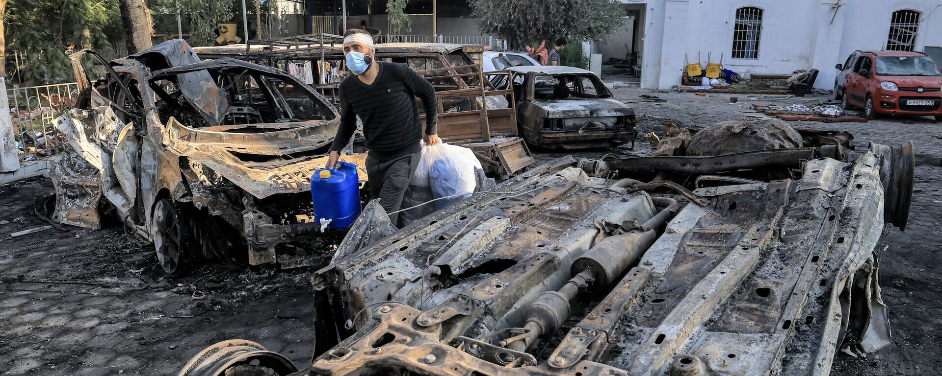 A man walks with salvaged items past destroyed vehicles at the site of the Ahli Arab hospital in central Gaza on October 18, 2023 in the aftermath of an overnight strike there.  - Sputnik International, 1920, 20.10.2023