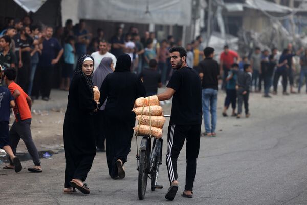 A man carries bags of food on a bicycle in the aftermath of Israeli strikes in Gaza City. Israeli air strikes destroyed hundreds of buildings in the Gaza Strip overnight, the civil defense service in the Hamas-controlled Palestinian territory said on October 28.  - Sputnik International