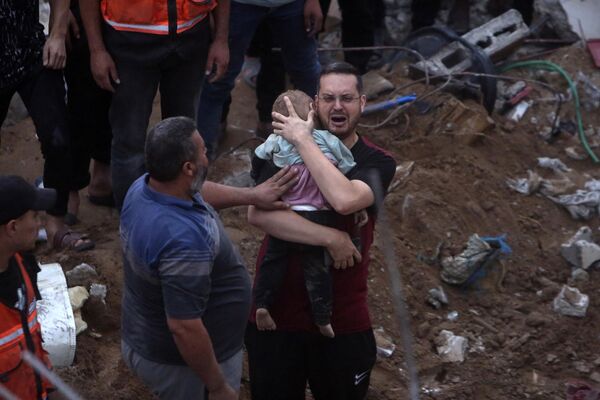 A distraught Palestinian man holding a dead child who was found under the rubble of a demolished building following Israeli airstrikes on the Nusseirat refugee camp, in the central Gaza Strip.  - Sputnik International