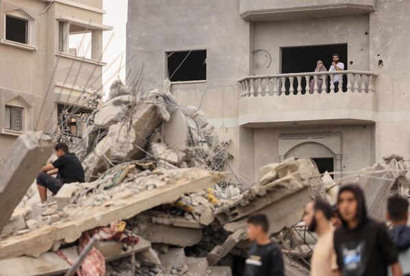 A couple looks on from the balcony of a damaged house as people glance at the ruins after an Israeli bombardment of Khan Yunis in the southern Gaza Strip. - Sputnik International