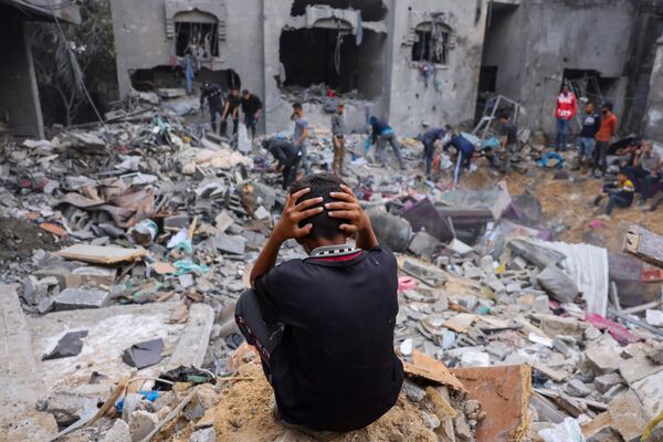 A distressed youth sits on debris as people rummage through the rubble of a demolished building after airstrikes on Rafah in the southern Gaza Strip. - Sputnik International
