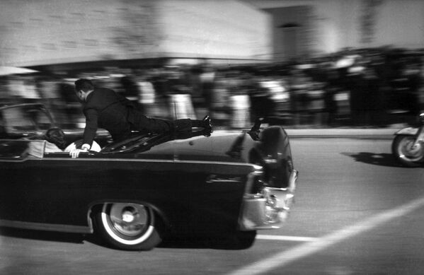 The limousine carrying mortally wounded President John F. Kennedy races toward the hospital seconds after he was shot in Dallas. With secret service agent Clinton Hill riding on the back of the car, Mrs. John Connally, wife of the Texas governor, bends over her wounded husband, and Mrs. Kennedy leans over the president. - Sputnik International