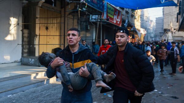 A Palestinian man carries an injured boy following the resumption of Israeli bombardment in Rafah, southern Gaza Strip, on December 1, 2023. - Sputnik International