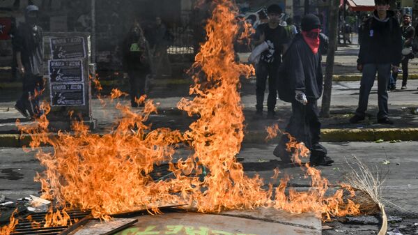 Demonstrators block a street with a barricade set on fire during a protest to commemorate the third anniversary of a social uprising against rising utility prices, in the surroundings of the Baquedano square in Santiago, on October 18, 2022 - Sputnik International