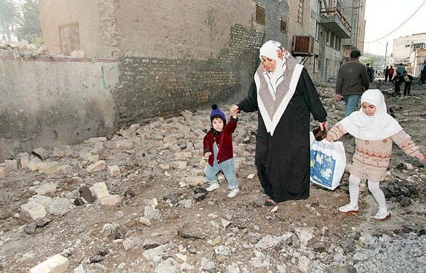 An Iraqi woman helps her children step over the rubble left after overnight US and British airstrikes on Baghdad.  - Sputnik International