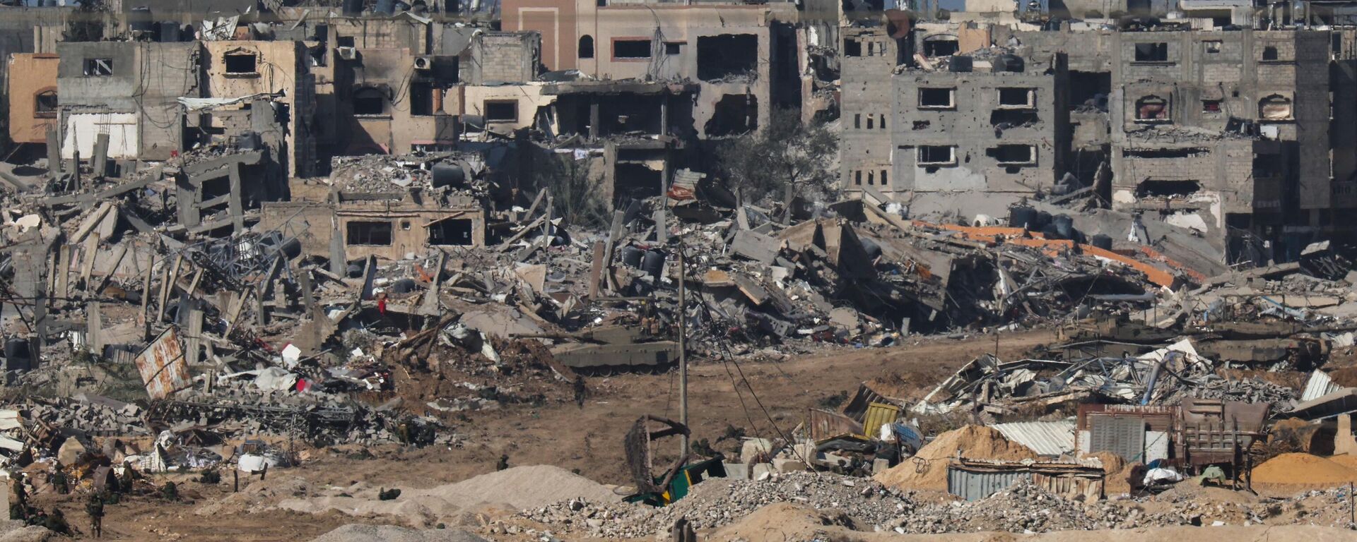 A picture taken from southern Israel bordering the Gaza Strip on December 22, 2023, shows an Israeli army tank rolling past debris of buildings in the Gaza Strip. - Sputnik International, 1920, 05.01.2024