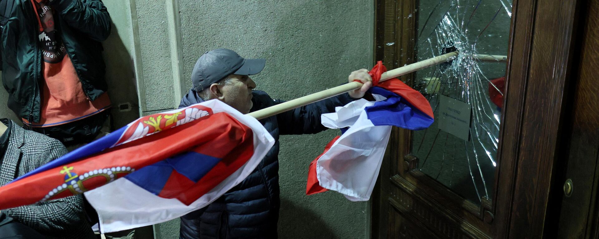Protester attempts to smash the window of a door leading inside Belgrade's city council during violent demonstrations December 24, 2023 protesting the results of recent parliamentary elections. - Sputnik International, 1920, 25.12.2023
