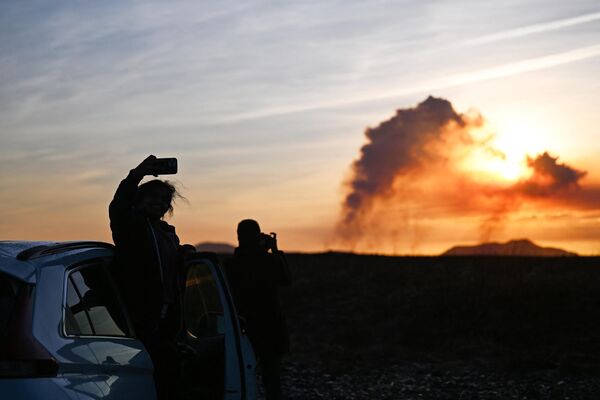People standing next to their car near Keflavik taking pictures as the plumes of smoke rise during the volcanic eruption. - Sputnik International