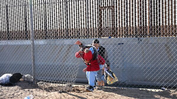 A family of migrants from Columbia climbs up through a canal fence after crossing under a hole in the US-Mexico border wall in El Paso, Texas, on December 19, 2022 - Sputnik International