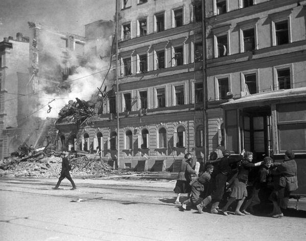 The streets of Leningrad after a Nazi air raid. Residents of the besieged city move a tram car from the facade of the destroyed house.  - Sputnik International