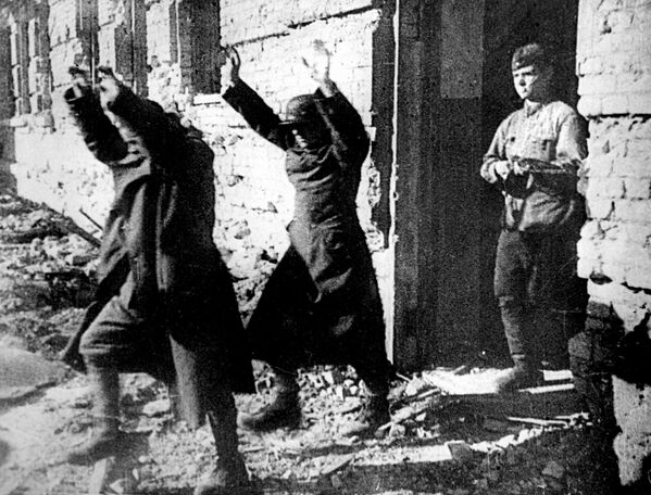 Two surrendering Axis troops, holding their hands up, are marched out of a war-ravaged building by one of their Russian captors as the Third Reich&#x27;s soldiers face defeat in Stalingrad. - Sputnik International