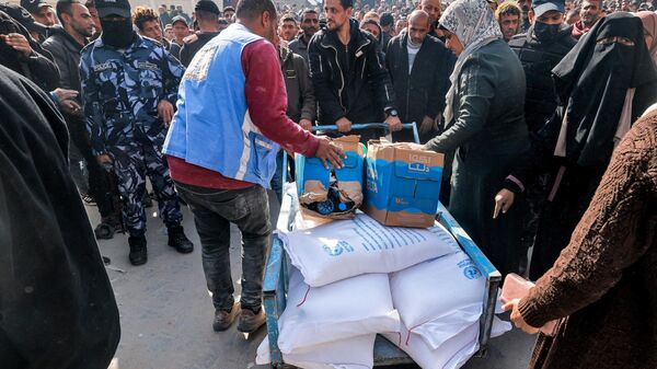 Workers of the United Nations Relief and Works Agency for Palestine Refugees (UNRWA) hand out flour rations and other supplies to people at an UNRWA warehouse in Rafah in the southern Gaza Strip on December 12, 2023, amid continuing battles between Israel and the militant group Hamas - Sputnik International