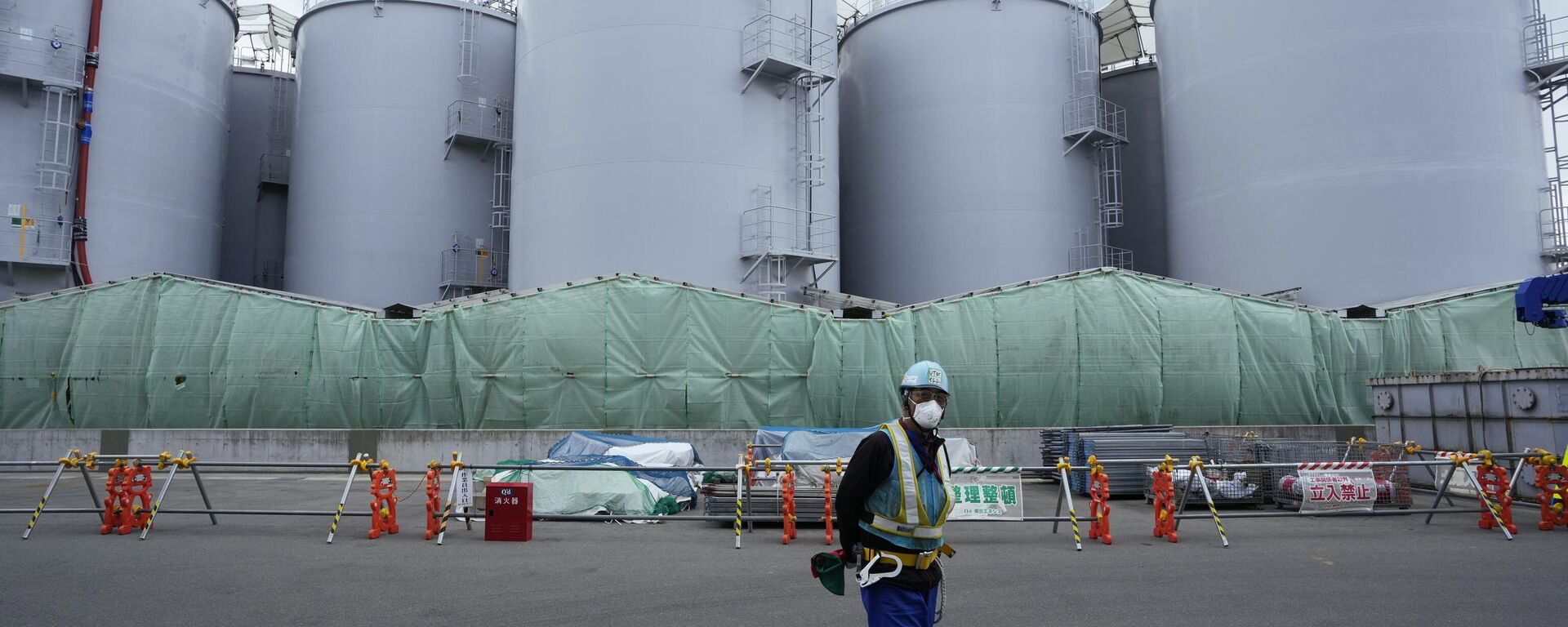 A worker helps direct a truck driver as he stands near tanks used to store treated radioactive water after it was used to cool down melted fuel at the Fukushima Daiichi nuclear power plant, run by Tokyo Electric Power Company Holdings (TEPCO) - Sputnik International, 1920, 08.02.2024