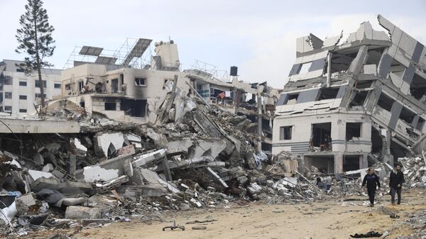 Palestinians walk past the building destroyed in the Israeli Bombardment of the Gaza Strip in Gaza City on Wednesday, Jan. 3, 2024 - Sputnik International