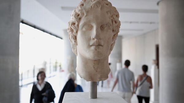 Visitors walk behind an ancient marble head of ancient Greek warrior-king Alexander the Great, displayed at the Acropolis museum in Athens, Oct. 12, 2014. Alexander the Great was one of the world's most successful military commanders, who enlarged his father's kingdom to include an empire stretching from modern Greece to India. During his youth, Alexander was tutored by the ancient Greek philosopher Aristotle until the age of 16.  - Sputnik International