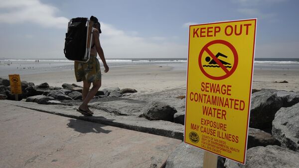 A beachgoer walks past a sign posted to warn people of contaminated water at Torrey Pines State Beach in San Diego Friday Sept. 9, 2011 - Sputnik International