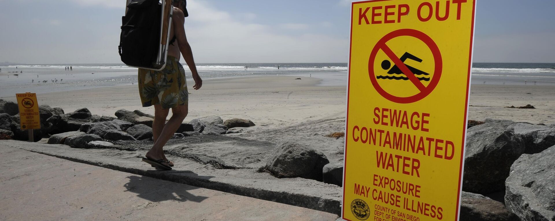 A beachgoer walks past a sign posted to warn people of contaminated water at Torrey Pines State Beach in San Diego Friday Sept. 9, 2011 - Sputnik International, 1920, 18.02.2024