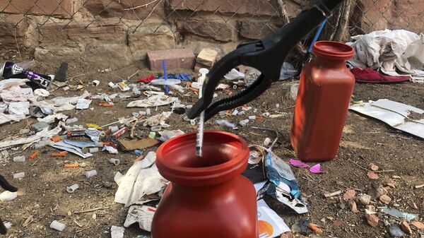 In this Aug. 9, 2019, file photo, a drug syringe found behind a vacant property in northeast Albuquerque, N.M., is placed into a container, as crews attempt to clear the lot of needles and other heroin paraphernalia. - Sputnik International