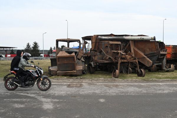 A motorcycle passes by destroyed Ukrainian agricultural vehicles at the Krakovets border crossing. - Sputnik International