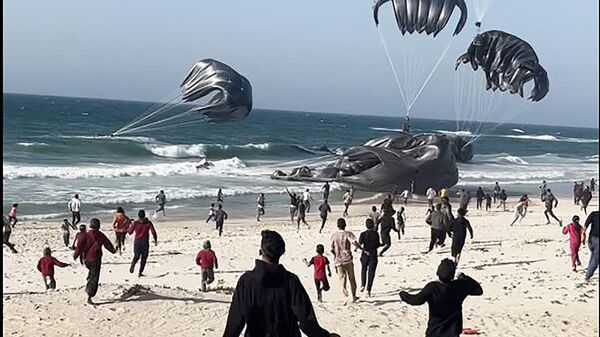  Palestinians running toward parachutes attached to food parcels, airdropped from US aircrafts on a beach in the Gaza Strip on March 2, 2024. - Sputnik International
