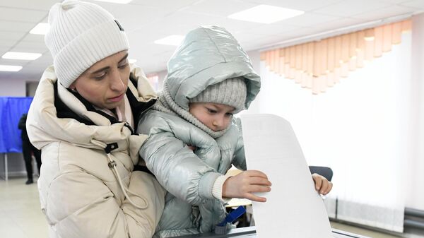 A woman with a child casts her ballot at a polling station during the presidential election in Kirovskoye - Sputnik International