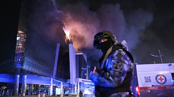 A law enforcement officer is seen near the burning Crocus City Hall concert venue following a reported shooting incident near Moscow, Russia. - Sputnik International