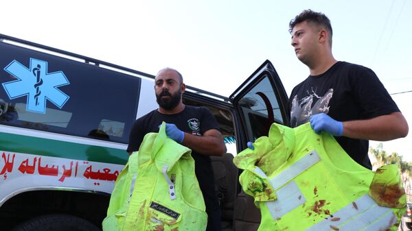 Comrades of four paramedics of the Lebanese Amal Movement civil defence teams, wounded after their ambulances were hit in a strike in the town of Tayr Harfa, show their blood-stained flak jackets outside a hospital in the southern Lebanese coastal city of Tyre on November 5, 2023 - Sputnik International