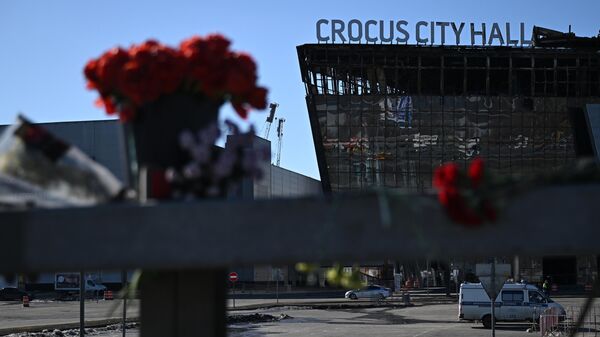 Flowers and toys are placed on the roadside in front of the burnt-out Crocus City Hall following a terrorist attack on the concert venue in Moscow Region, Russia. - Sputnik International