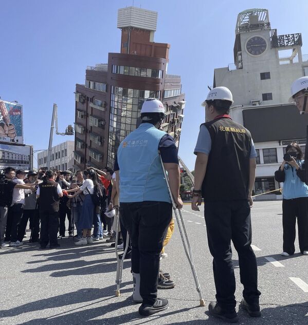 Government workers and journalists are seen near firefighters working near a leaning building in the aftermath of an earthquake in Hualien, eastern Taiwan.  - Sputnik International