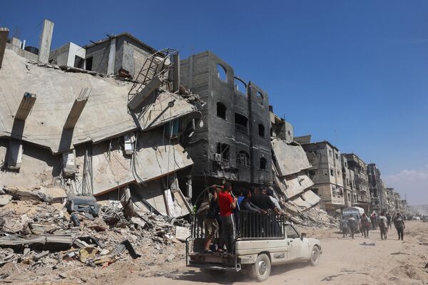 Palestinians drive by devastated buildings in Khan Yunis. - Sputnik International